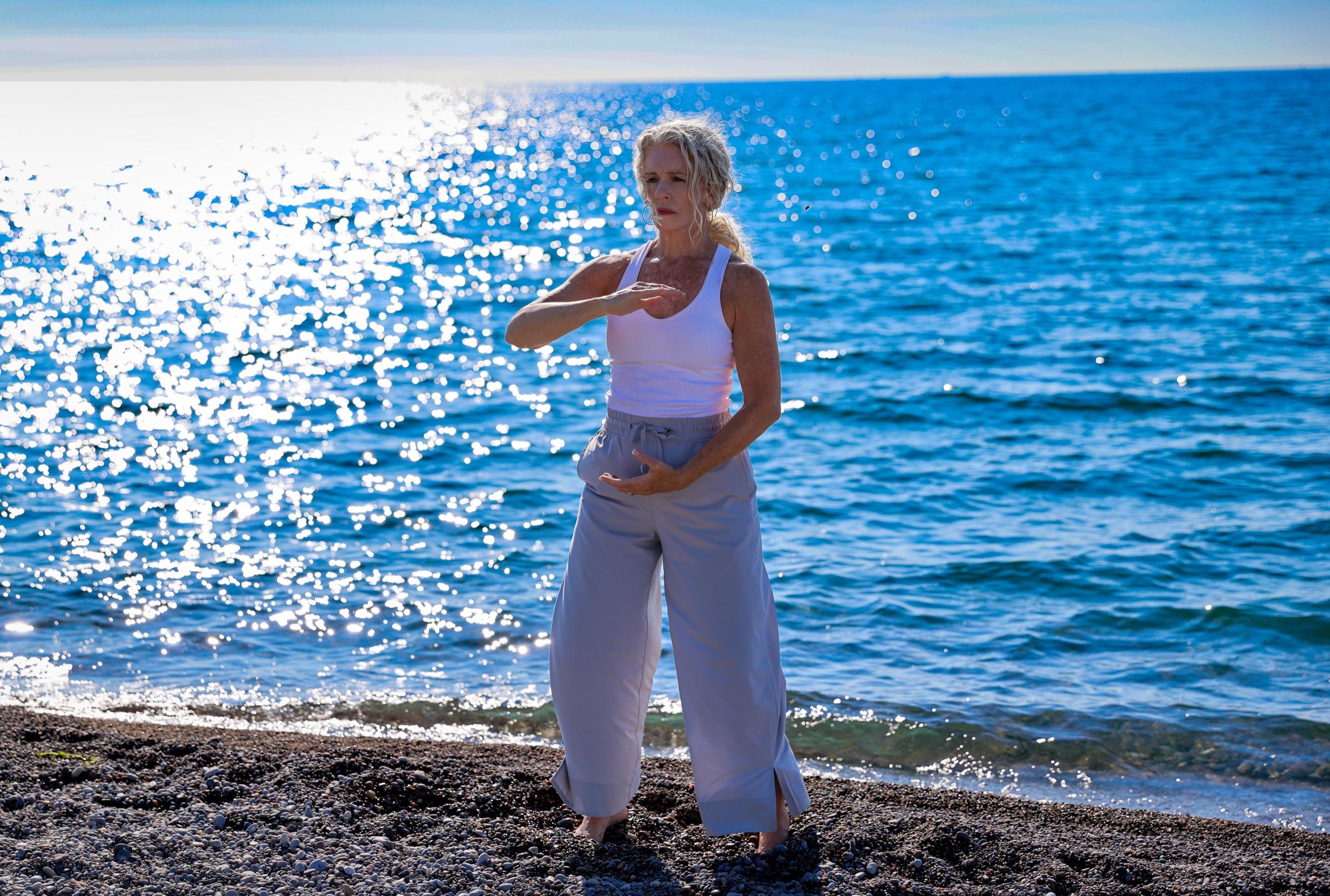 Stephanie standing at the shoreline, hands drifting through a gentle flowing movement